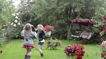 Children have fun in the rain. Two sisters are running around having fun in the rain in the yard at home. video