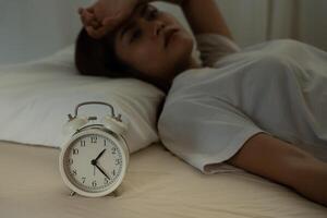 asian woman in bed late trying to sleep suffering insomnia, sleepless or scared in a nightmare, looking sad worried and stressed. Tired and headache or migraine waking up in the middle of the night. photo