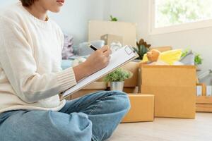 Move house, relocation. Woman using household checklist for new apartment Inside the room are cardboard boxes containing personal belongings and furniture. Move into a house or condominium photo
