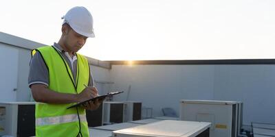 Asian maintenance engineer works on the roof of factory. contractor inspect compressor system and plans installation of air condition systems in construction. Checklist, inspector, control photo