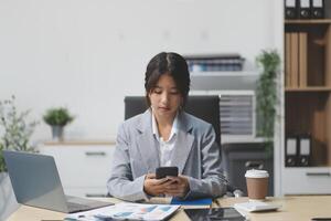 Asian businesswoman in formal suit in office happy and cheerful during using smartphone and working photo
