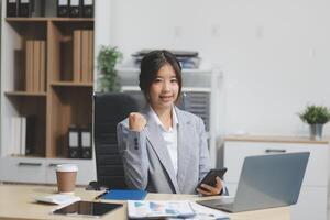 Asian businesswoman in formal suit in office happy and cheerful during using smartphone and working photo