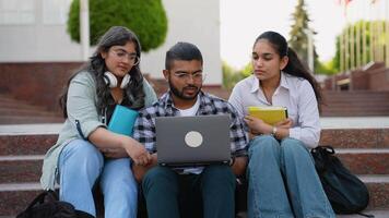 Happy Indian student using laptop while studying with female friends in front of university building video