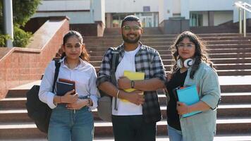 Three Indian students posing in front of university, looking at camera and smiling video