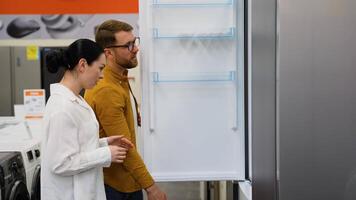 Couple open door of the refrigerator in the hardware electronics store and compare with other models video