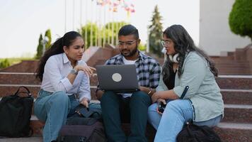 Happy Indian student using laptop while studying with female friends in front of university building video