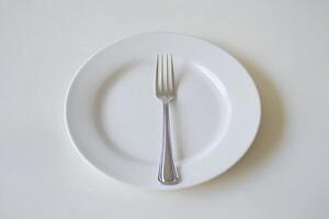 A single fork rests on a white plate, symbolizing emptiness or a fresh start. photo