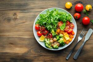 A healthy and colorful salad with grilled chicken, broccoli, tomatoes, and pumpkin on a wooden table. photo