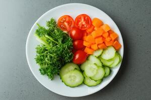 A plate of fresh vegetables, including cucumber, carrot, parsley, and cherry tomatoes. photo