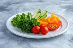 A plate of fresh vegetables, including cucumbers, cherry tomatoes, bell peppers and parsley. photo