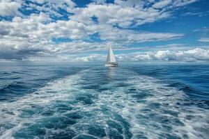 Sailboat sailing on a clear blue ocean with white foamy wake in the foreground and fluffy clouds in the sky. photo