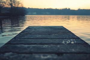 Wooden dock extending into still lake water with a sunset in the background. photo