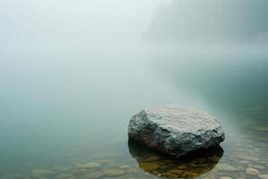 A single rock protrudes from a misty lake. photo