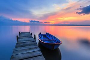 A small blue boat sits on a wooden dock at sunset. photo