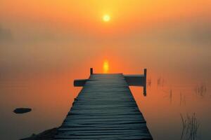 A wooden pier extends into a misty lake at sunrise, with the sun shining through the fog. photo