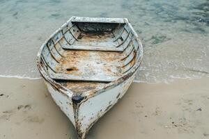 An old, white wooden boat sits beached on a sandy shore with the gentle waves of the ocean lapping at its bow. photo
