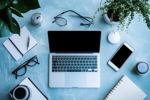 Flat lay of laptop, phone, and office supplies on a blue desk. photo