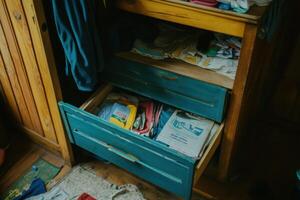 Open drawer of a wooden cabinet with clothes and other items inside. photo
