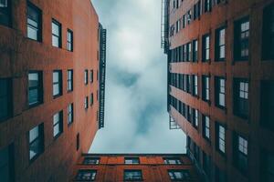 Two brick buildings with windows frame a cloudy sky viewed from below. photo