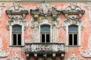 Ornate windows and balcony on a pink building facade. photo