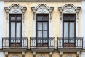 Three windows with balconies on a yellow building. photo