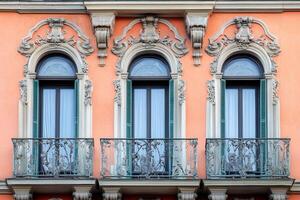 Three ornate windows with balconies on a peach building facade. photo