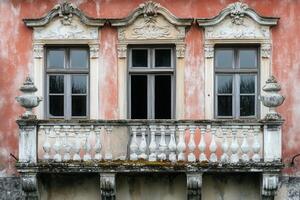 Three windows with ornate trim and a balcony on a pink building. photo