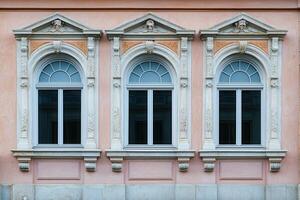 Three arched windows with ornate frames on a pink building facade. photo