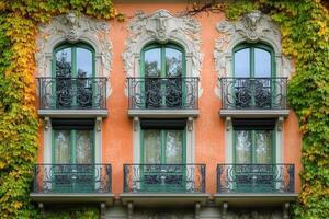 Three ornate balconies with green windows and railings on an orange building covered in ivy. photo