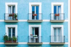 A blue building with six windows and balconies with plants. photo