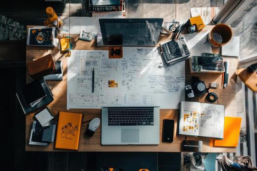Overhead view of a messy desk with a laptop, notebooks, a camera, and a drawing. photo