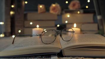 A tranquil reading nook features an open book with eyeglasses resting on its pages. Soft candlelight and fairy lights create a warm atmosphere, perfect for evening reading. video