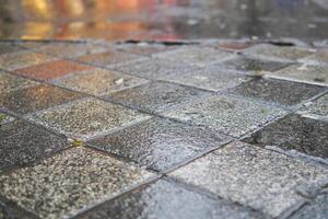 A wet, paved surface exhibiting highly reflective tiles during rainy weather conditions photo