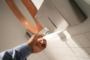 Hand Using Paper Towel Dispenser in a Hygienic Public Restroom with Clean White Tiles photo
