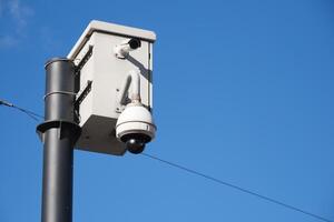 A surveillance camera is firmly mounted on a pole, set against a clear blue sky backdrop photo