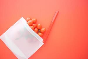 Fresh Cherry Tomatoes Displayed in a Transparent Bag Sitting Next to a Straw on a Vibrant Background photo