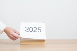 Business woman hand change 2025 Year Calendar on table in office background. countdown, Happy New Year, Resolution, Year End and New Start and Goals Plan Action Concept photo