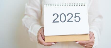 Business woman hand holding and change 2025 Year Calendar on white background table in office. countdown, Happy New Year, Resolution, Year End and New Start and Goals Plan Action Concept photo
