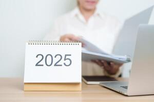 2025 Year Calendar on table with business woman using laptop computer, working and writing in office. countdown, Happy New Year, Resolution, Year End and New Start and Goals Plan Action Concept photo