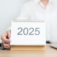 2025 Year Calendar on table with business woman using laptop computer, working and writing in office. countdown, Happy New Year, Resolution, Year End and New Start and Goals Plan Action Concept photo