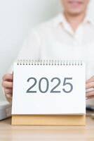 2025 Year Calendar on table with business woman using laptop computer, working and writing in office. countdown, Happy New Year, Resolution, Year End and New Start and Goals Plan Action Concept photo