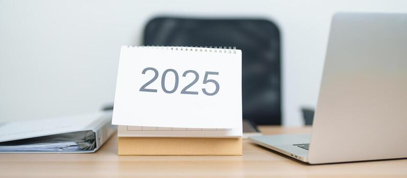 2025 año calendario en mesa con ordenador portátil computadora durante trabajando y escritura en oficina. cuenta regresiva, contento nuevo año, resolución, año final y nuevo comienzo y metas plan acción concepto foto