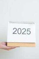 Business woman hand holding and change 2025 Year Calendar on white background table in office. countdown, Happy New Year, Resolution, Year End and New Start and Goals Plan Action Concept photo