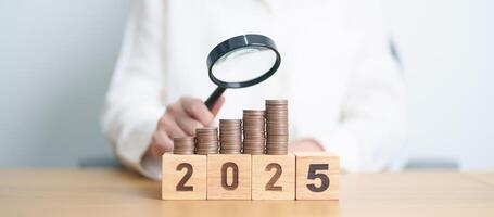 Happy New Year 2025 with coins money stack growing with magnifier glass. Money saving, Inflation, tax, cash flow, Job search, hiring and research development concepts photo