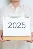 Business woman hand holding and change 2025 Year Calendar on white background table in office. countdown, Happy New Year, Resolution, Year End and New Start and Goals Plan Action Concept photo