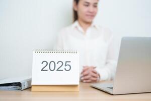 2025 Year Calendar on table with business woman using laptop computer, working and writing in office. countdown, Happy New Year, Resolution, Year End and New Start and Goals Plan Action Concept photo