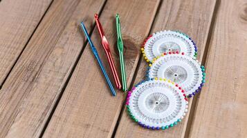 Set of colorful crochet hooks and several wheels of sewing pins arranged neatly on a wooden surface. photo