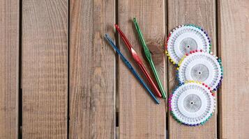 Set of colorful crochet hooks and several wheels of sewing pins arranged neatly on a wooden surface. photo
