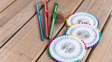 Set of colorful crochet hooks and several wheels of sewing pins arranged neatly on a wooden surface. photo