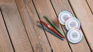 Set of colorful crochet hooks and several wheels of sewing pins arranged neatly on a wooden surface. photo